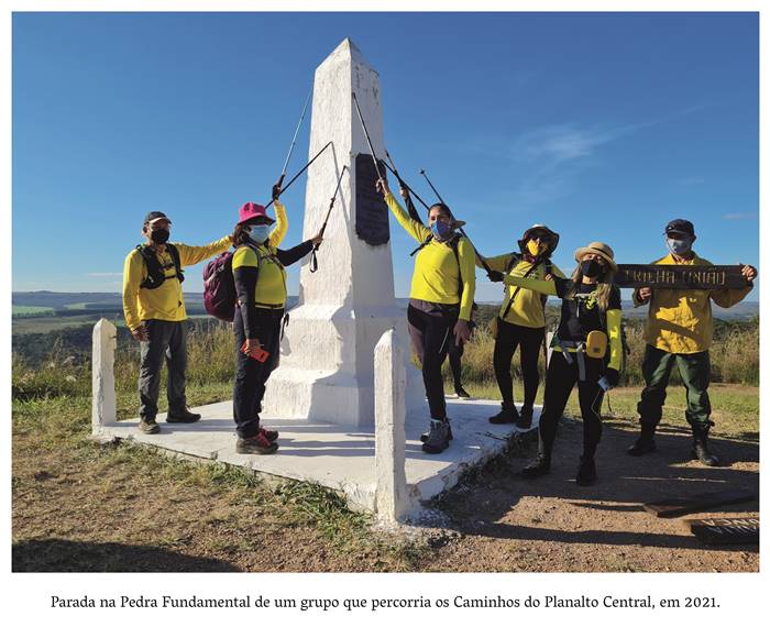 4 z 4- Parada na Pedra Fundamental de um grupo que percorria os Caminhos do Planalto Central, em 2021. Homens e mulheres trajando calças pretas e camisetas amarelas posam rente a pedra fundamental.
            Esses homens seguram uma espécie de espada que está encostado na pedra. Um homem segura uma placa onde está escrito: Trilha União. Realização: Academia Planaltinense de Letras, Artes e Ciências (APLAC), pelo Ecomuseu Pedra Fundamental e pelo Coletivo Nativo Audiodescrição produzida  pelo Instituto de Promoção das Pessoas com Deficiência Visual Audiodescritora: Elma Lúcia Rodrigues Consultor: Fernando Rodrigues Este projeto é promovido com recursos do Fundo de Apoio a Cultura do DF